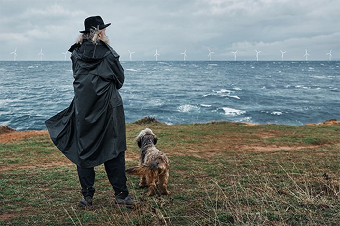 Man met hoed en hond die over zee kijkt naar een windpark op zee