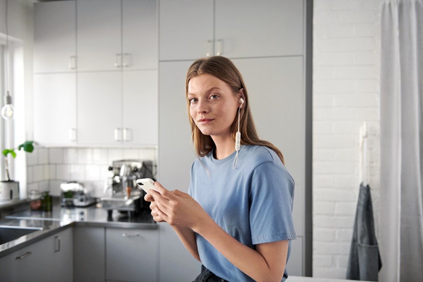 Jonge vrouw staat met mobiel in de hand in de keuken