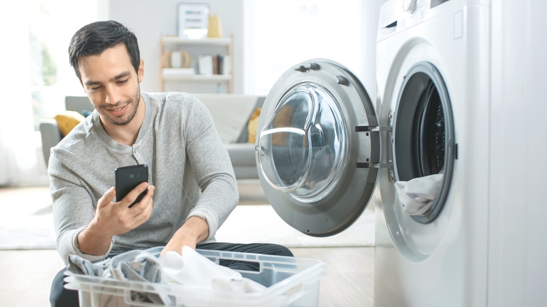 Man met telefoon bij wasmachine overweegt een energiecontract met dynamische prijzen