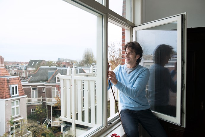 Man in blauw shirt in open raam om isolatie aan te brengen n.a.v. Energiescan