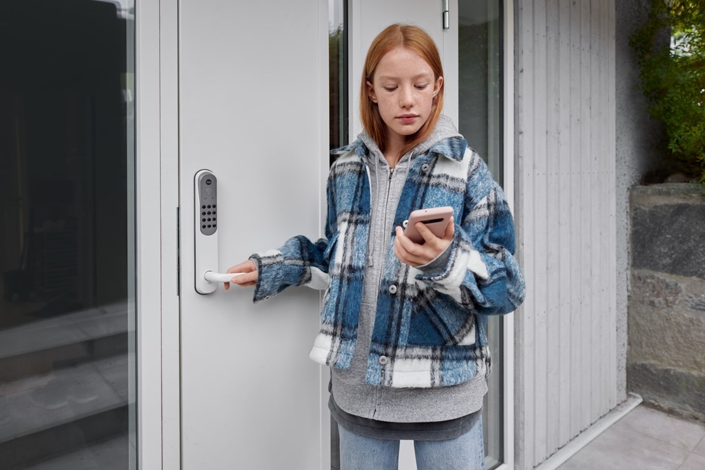 Meisje staat bij de voordeur met haar telefoon in de hand