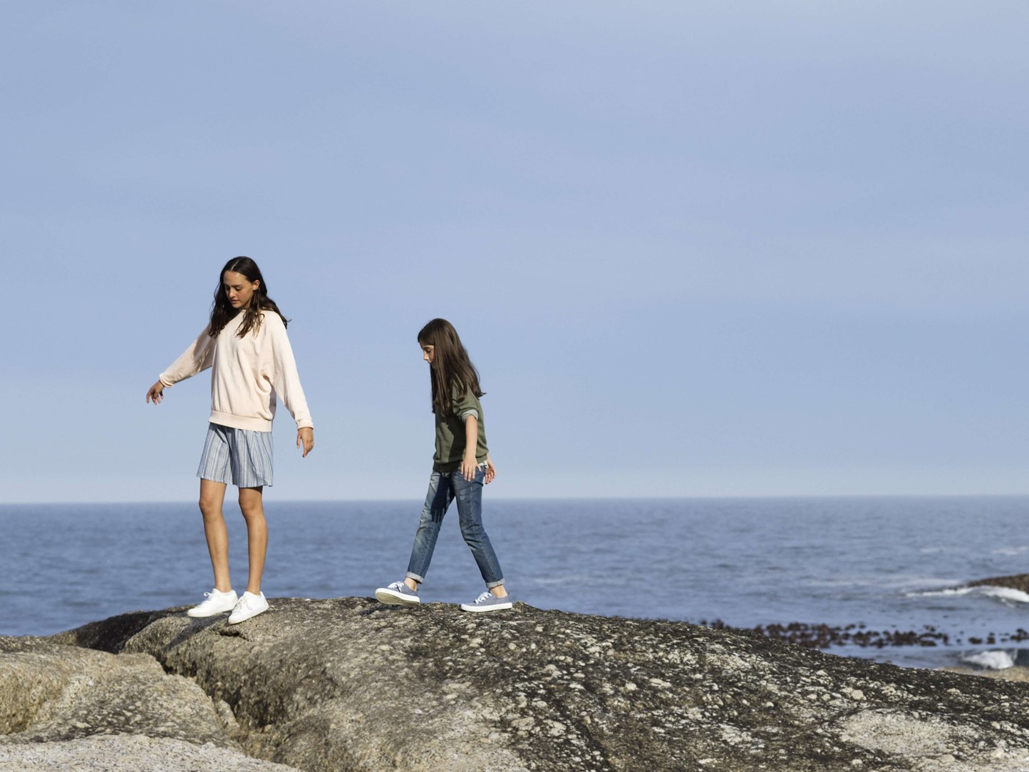 Twee meiden lopen voorzichtig op een grote rots aan de kust