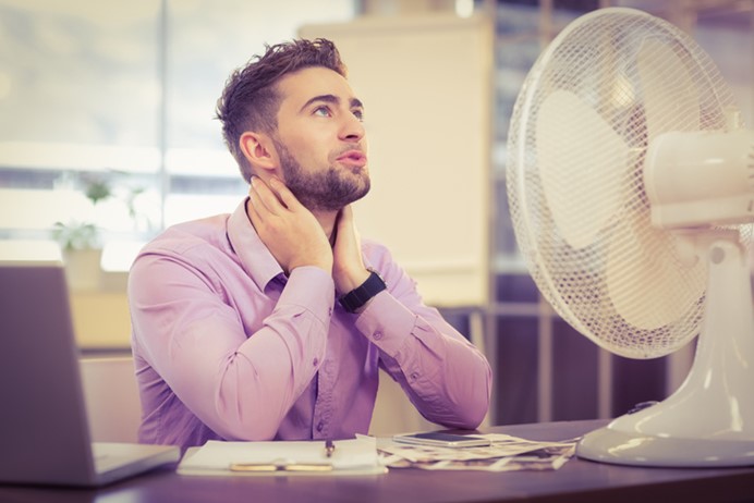 Man in roze overhemd met ventilator op het bureau - klimaatbeheersing op warme dagen