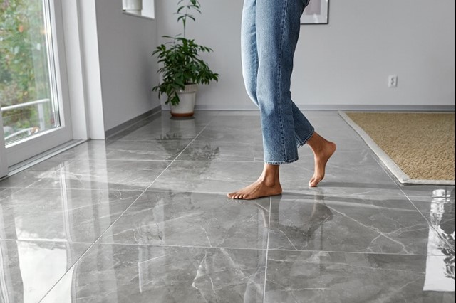 Vrouw in spijkerbroek met blote voeten op een glimmende stenen vloer in de woonkamer