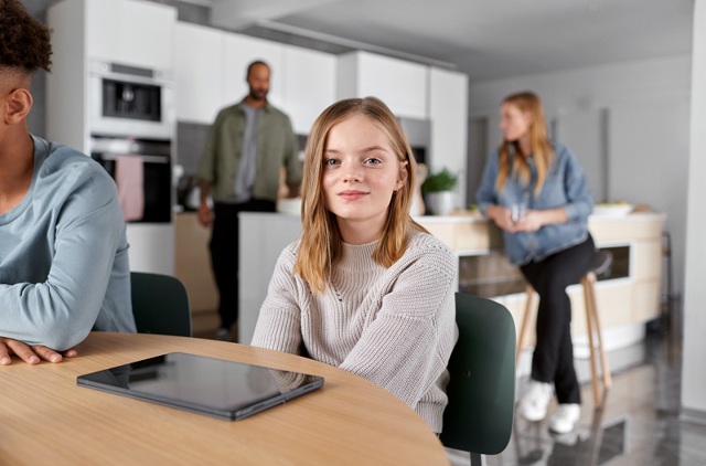 Vriendelijk meisje aan de keukentafel met familie en vrienden op de achtergrond | Vattenfall over gemiddeld energieverbruik