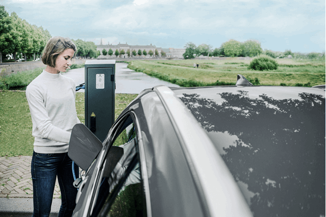 Vrouw laadt haar elektrische auto op aan de rand van een park  - Minder CO2-uitstoot elektrische auto
