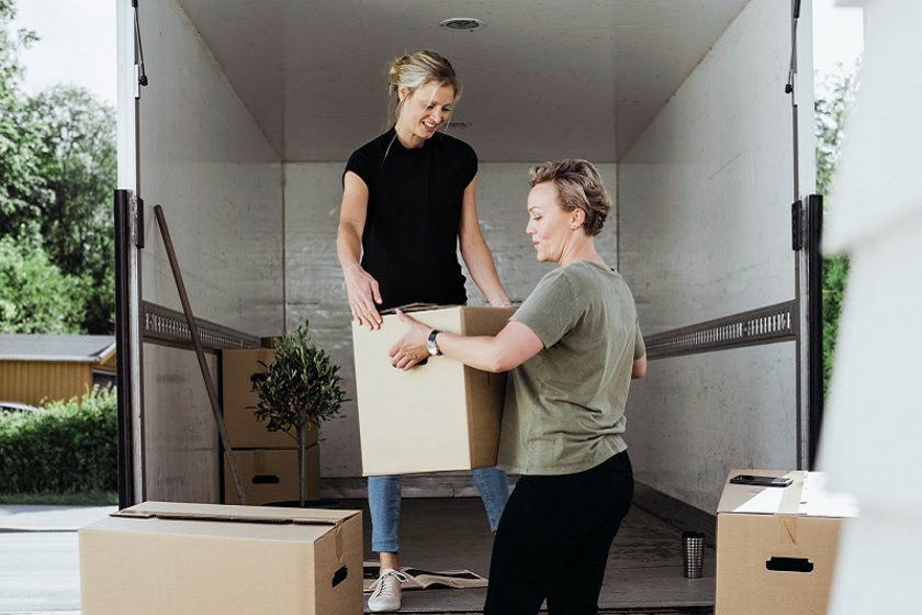 Twee vrouwen halen verhuisdozen uit een verhuiswagen