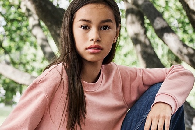 Jong meisje met roze sweater en lang bruin haar bij een boom