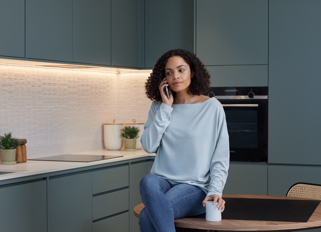 Vrouw met lichtblauwe trui en donker haar in moderne keuken aan het bellen - kosten stadsverwarming