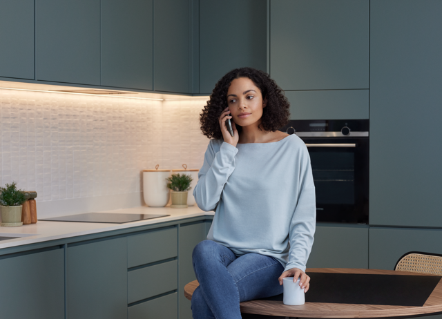 Vrouw met lichtblauwe trui en donker haar in moderne keuken aan het bellen - kosten stadsverwarming