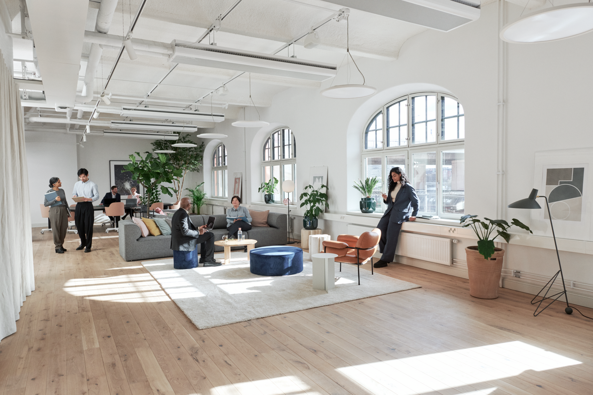 Goed geïsoleerd bedrijfspand met groepjes werknemers aan vergadertafel, zitje, staand en vensterbank