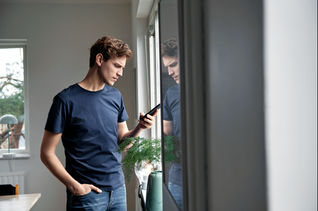 Jonge ondernemer met blauw t-shirt kijkt op zijn mobiel - Bespaar energiekosten in nieuw pand