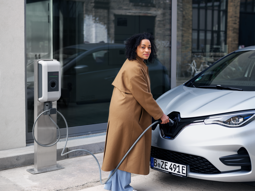 Een vrouw kijkt achterom terwijl ze haar auto oplaadt