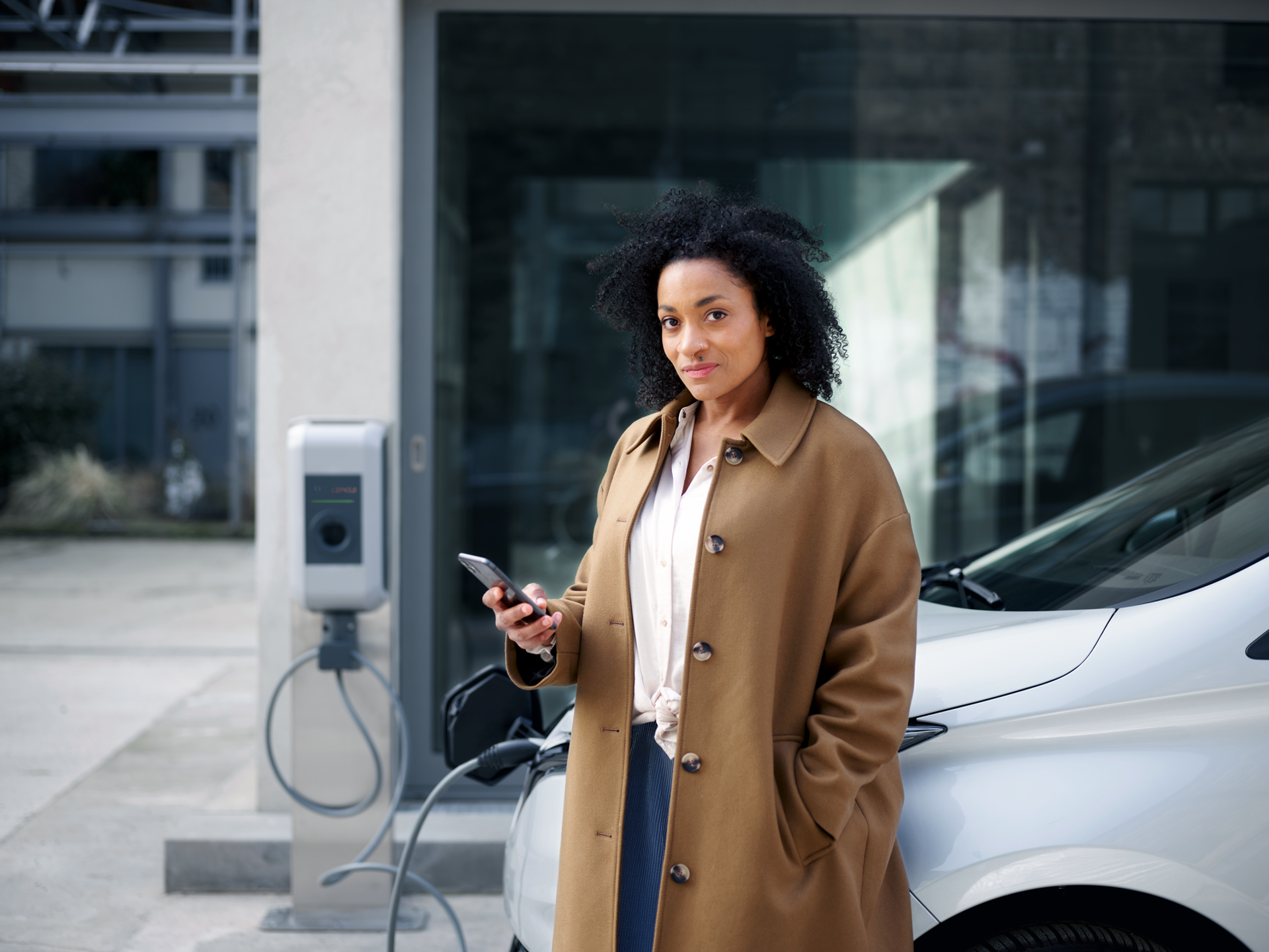 Een zzp'er leunt tegen haar auto terwijl ze die oplaadt