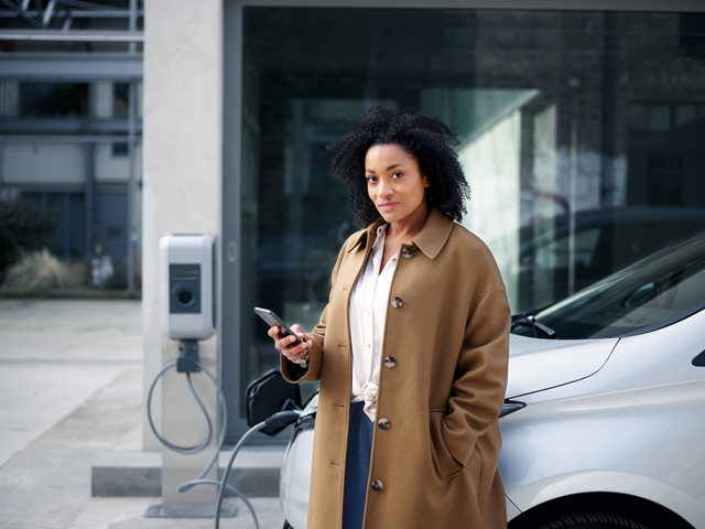 Een ondernemer kijkt op haar telefoon terwijl haar auto oplaadt