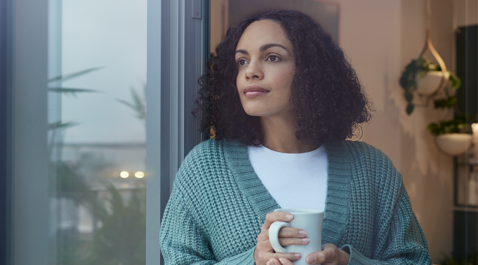 Vrouw staat met een kopje thee in haar hand en kijkt uit het raam