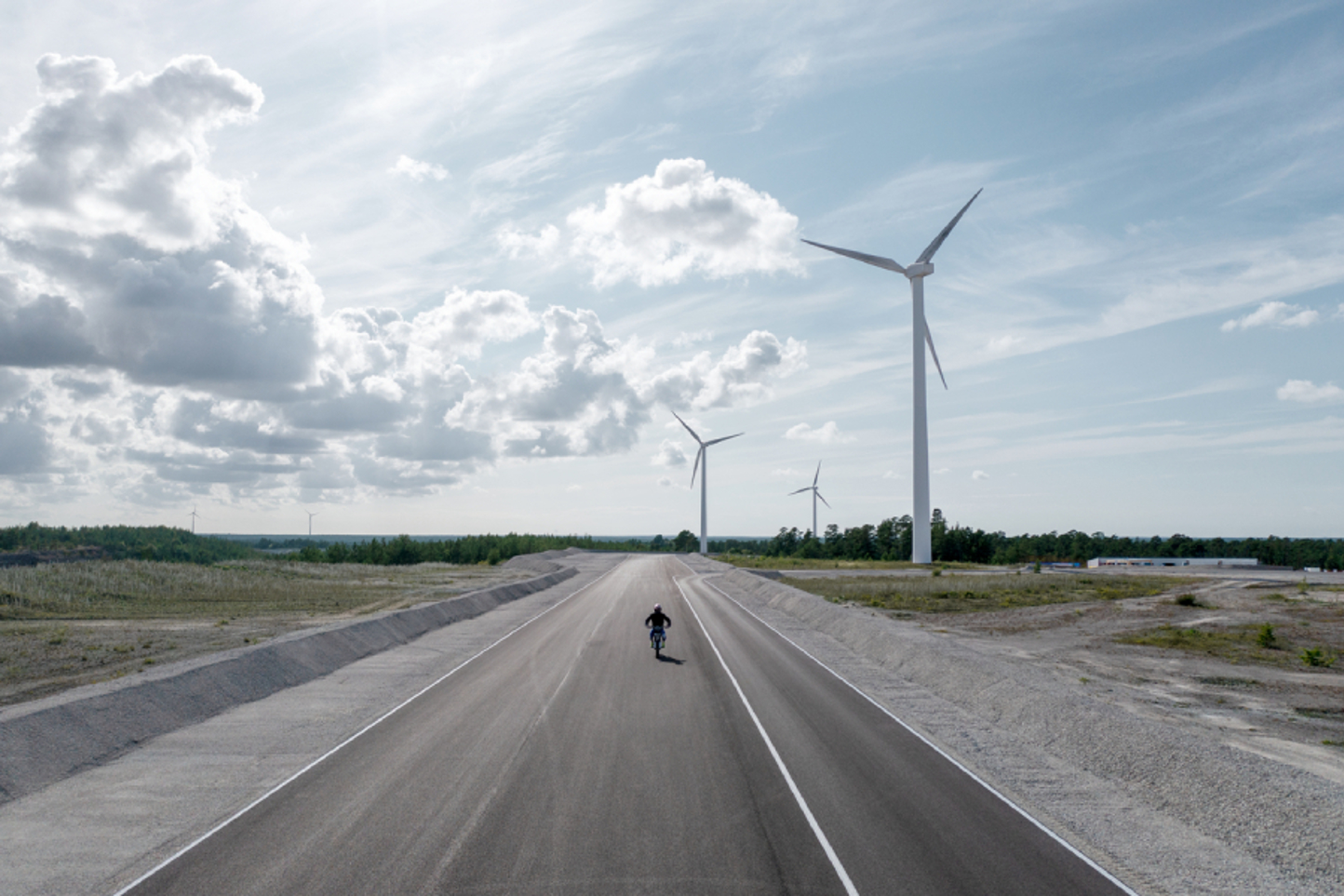 Iemand rijdt op een motor op een nieuwe weg in een veld met windmolens