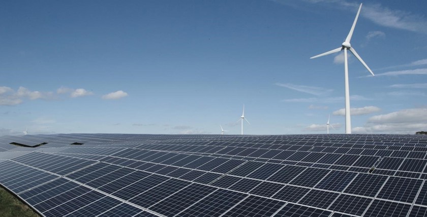 Veld met rijen zonnepanelen met op de achtergrond een aantal windmolens