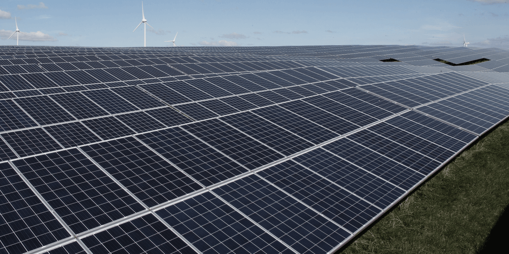 Zonnepanelen op land met op de achtergrond windmolens
