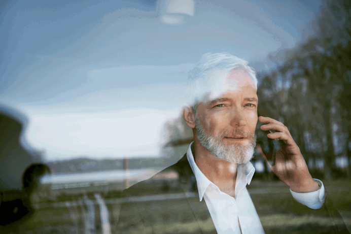 Man die door het raam kijkt met een mobiele telefoon in zijn hand