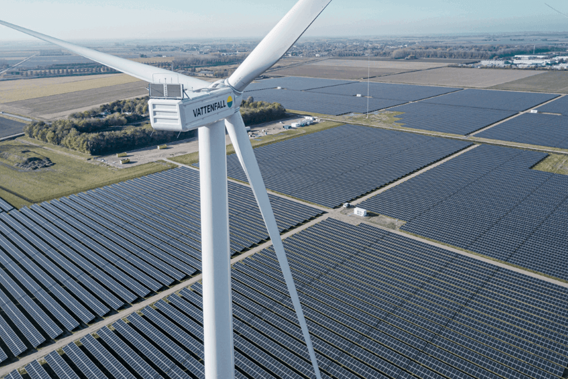 Luchtfoto van een windmolen met op de achtergrond een veld vol met zonnepanelen