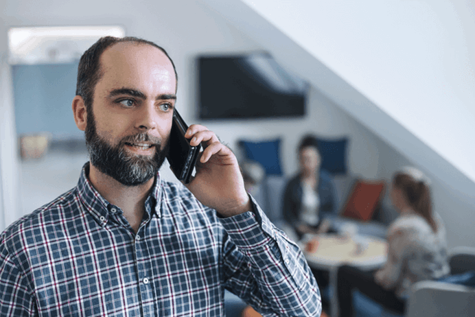 Man met baard in kantooromgeving belt met mobiele telefoon