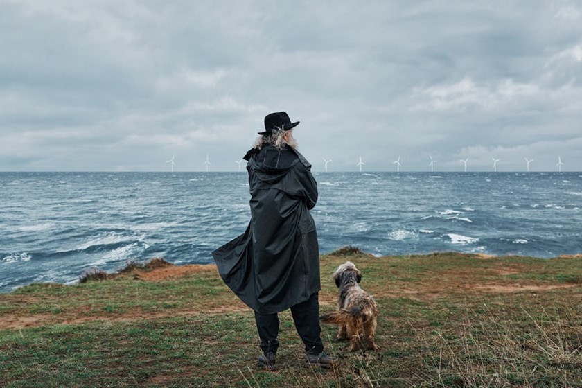 Man met hoed en hondje met op de achtergrond windmolens op zee