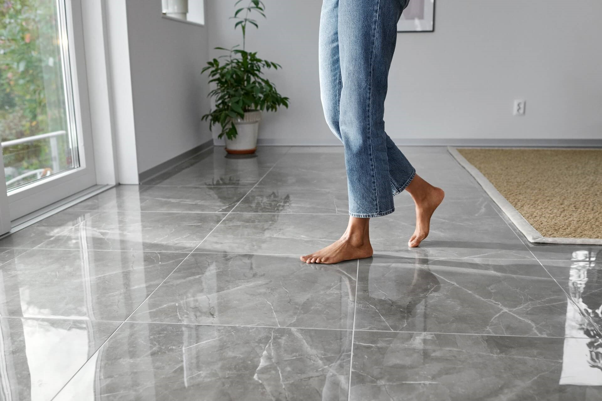 Vrouw in spijkerbroek met blote voeten op een glimmende stenen vloer in de woonkamer |  Info over boete overstappen energie
