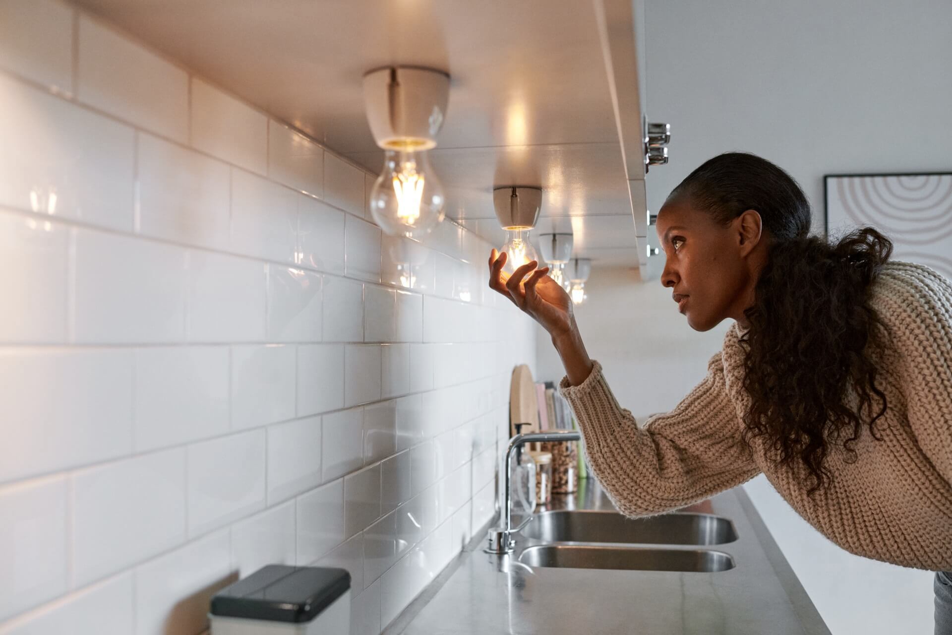 Vrouw met een lange paardestaart draait een nieuwe ledlamp in om het aanrechtblad te verlichten | Vattenfall over goedkope energie