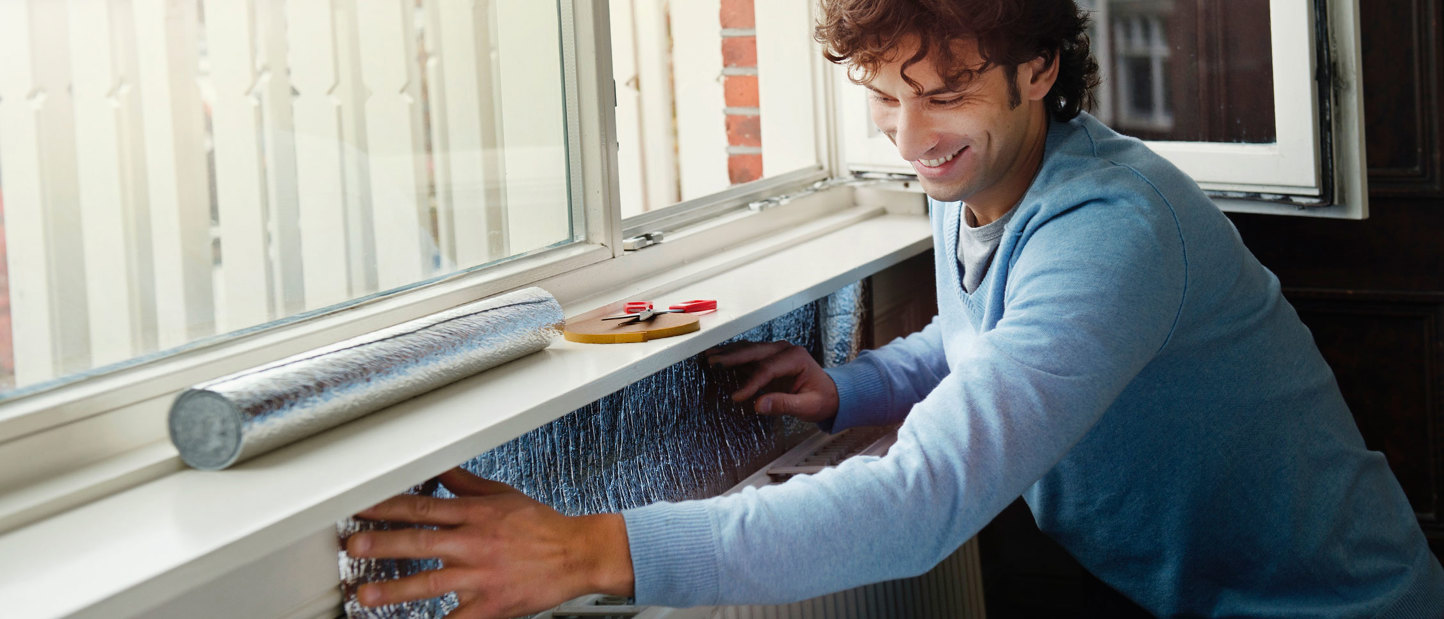 Jonge man brengt radiatorisolatie aan in zijn huis