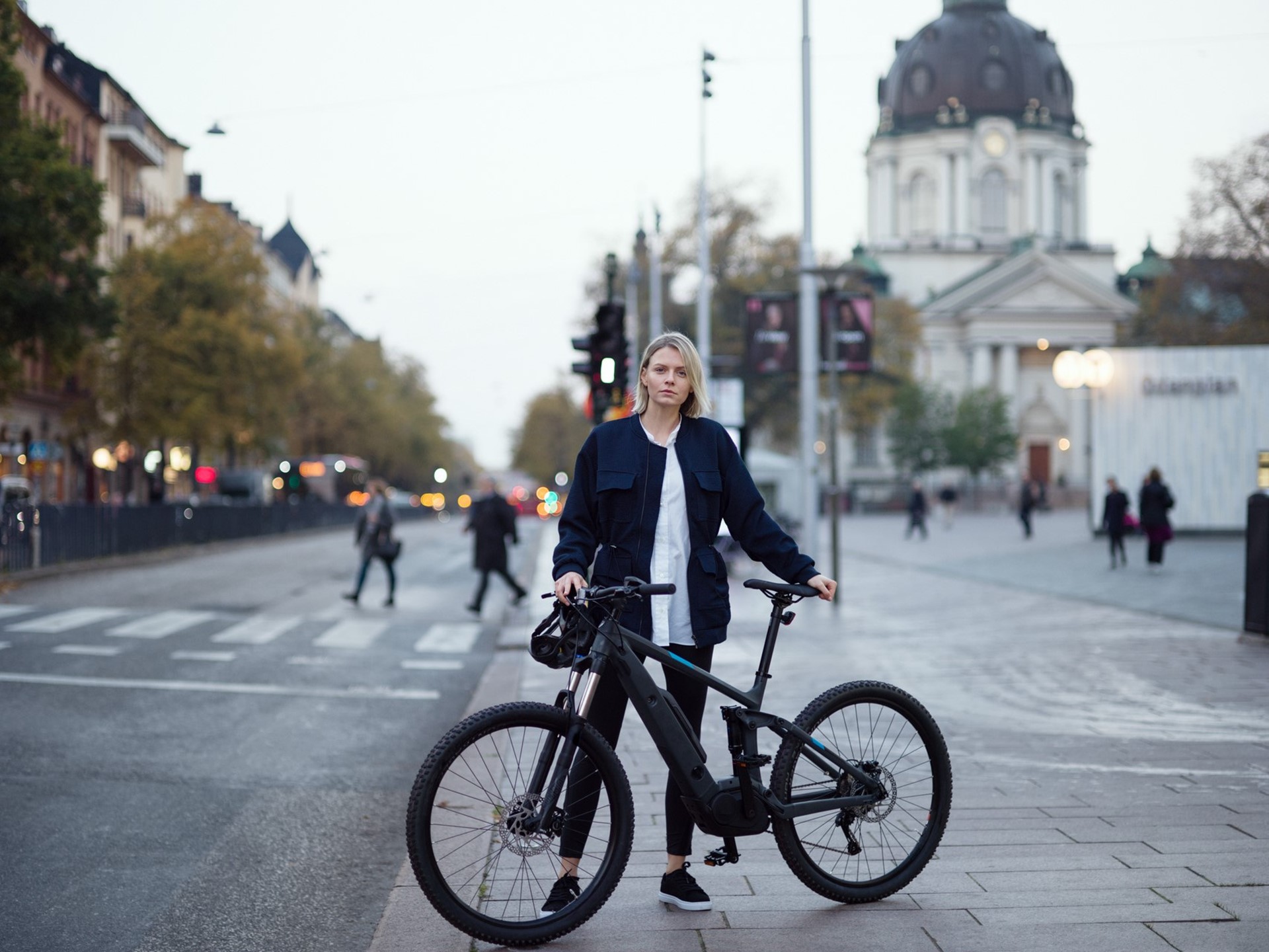 Vrouw staat met fiets in haar handen op de stoep in het centrum van een stad
