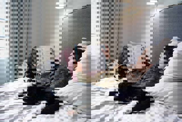 Vrouw leest een boek op bed met kat naast haar | Gas vergelijken