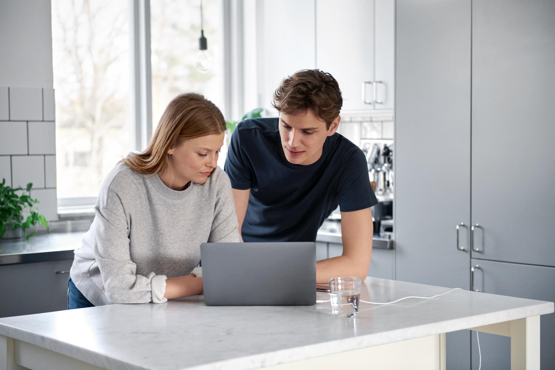 Jonge vrouw en man in hun keuken bekijken informatie over het prijsplafond op hun laptop