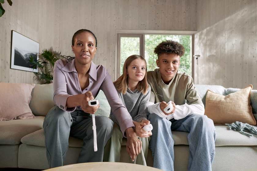 Vriendelijk lachende moeder met zoon en dochter op de bank spelen videospel