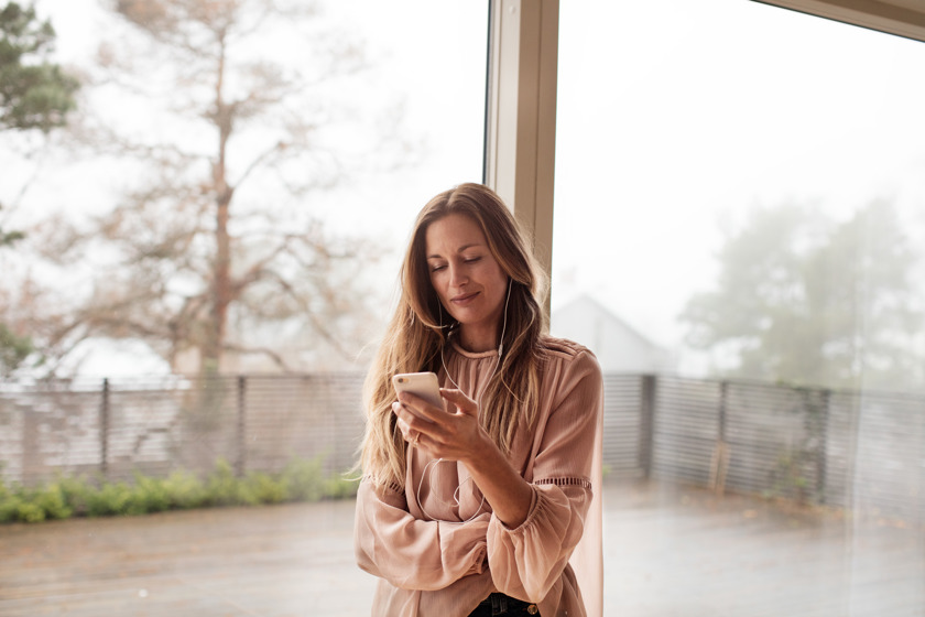 Vrouw met lang haar en mobiel in serre met uitzicht op houten terras