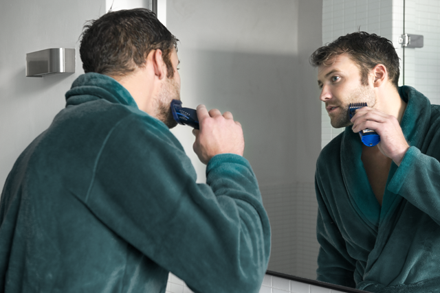Jonge man in groene badjas staat te scheren voor de spiegel | Vattenfall over gas water licht kosten