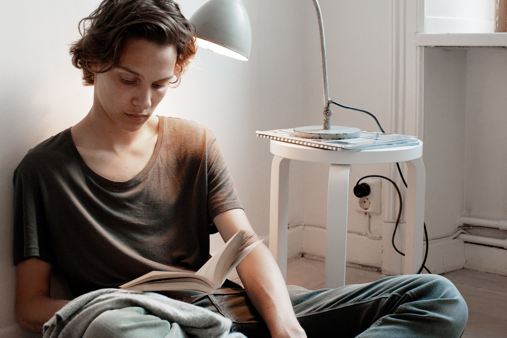 Jonge man met bruin t-shirt zit op de grond een boek te lezen over de kWh prijs