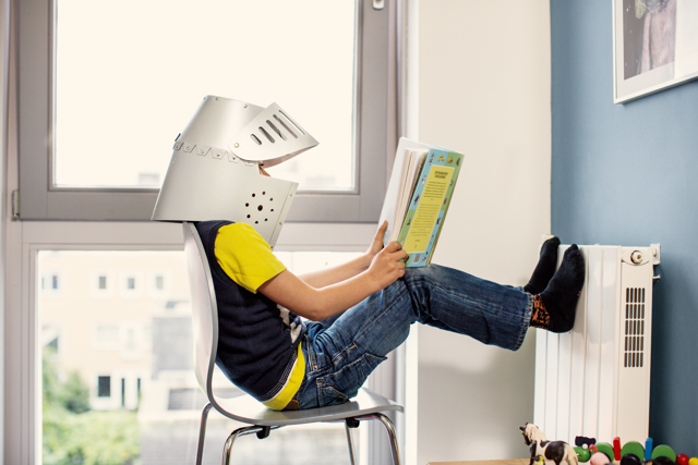 Jongetje met zelfgemaakte helm leest een spannend boek met zijn voeten tegen de radiator | Vattenfall over een radiatorventilator
