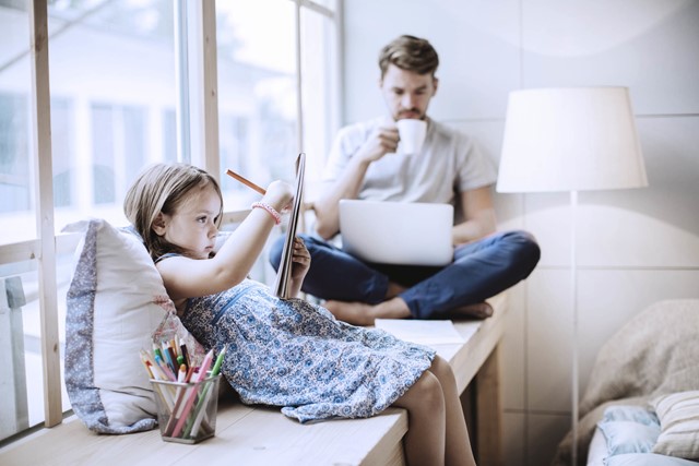 Meisje op bank aan het tekenen op een kladblok en vader drinkt koffie en kijkt op laptop | Vattenfall over energie