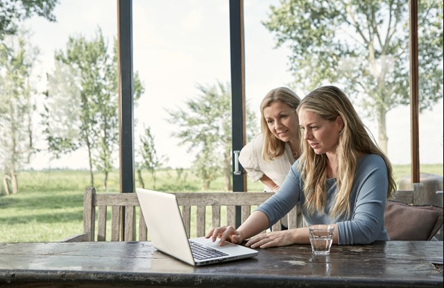 Moeder kijkt mee met dochter achter een laptop in de serre | Vattenfall energielabel opvragen