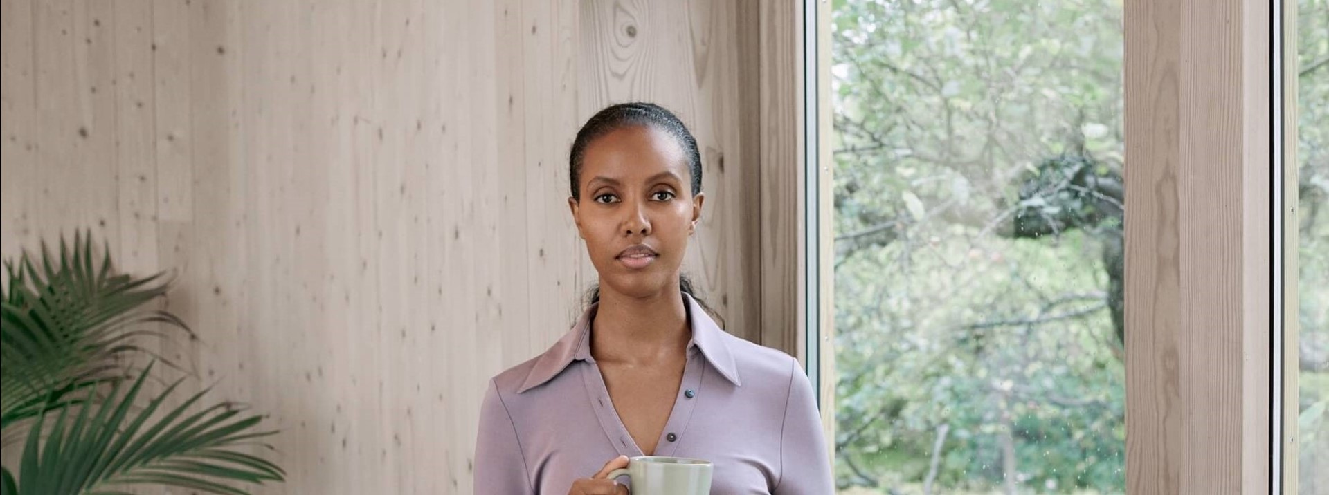 Zelfverzerkerde vrouw staat met een kop koffie voor een radiator bij het raam | De beste stroomleverancier