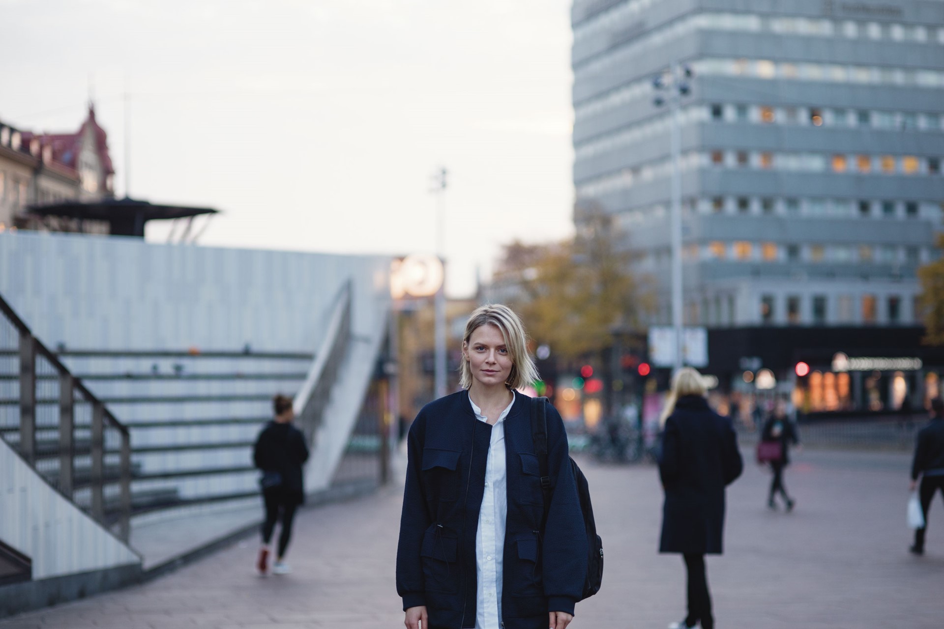 Jonge vrouw met blauwe jas op een plein met trappen - ISDE: subsidie op de verduurzaming van je bedrijf
