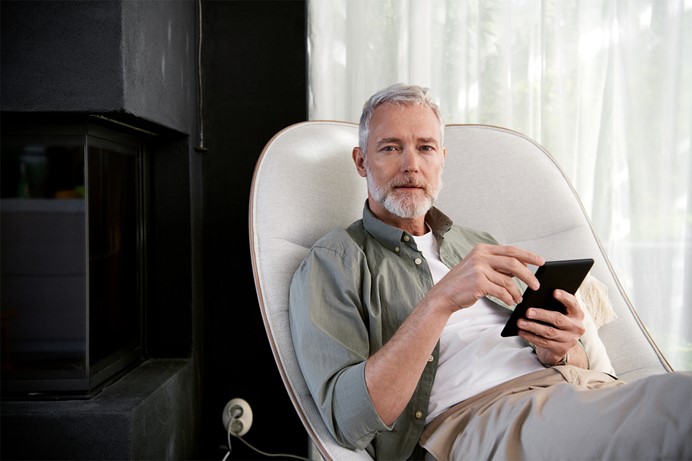 Man met grijs haar in luie stoel met tablet in de hand voor de Direct Besparen Check