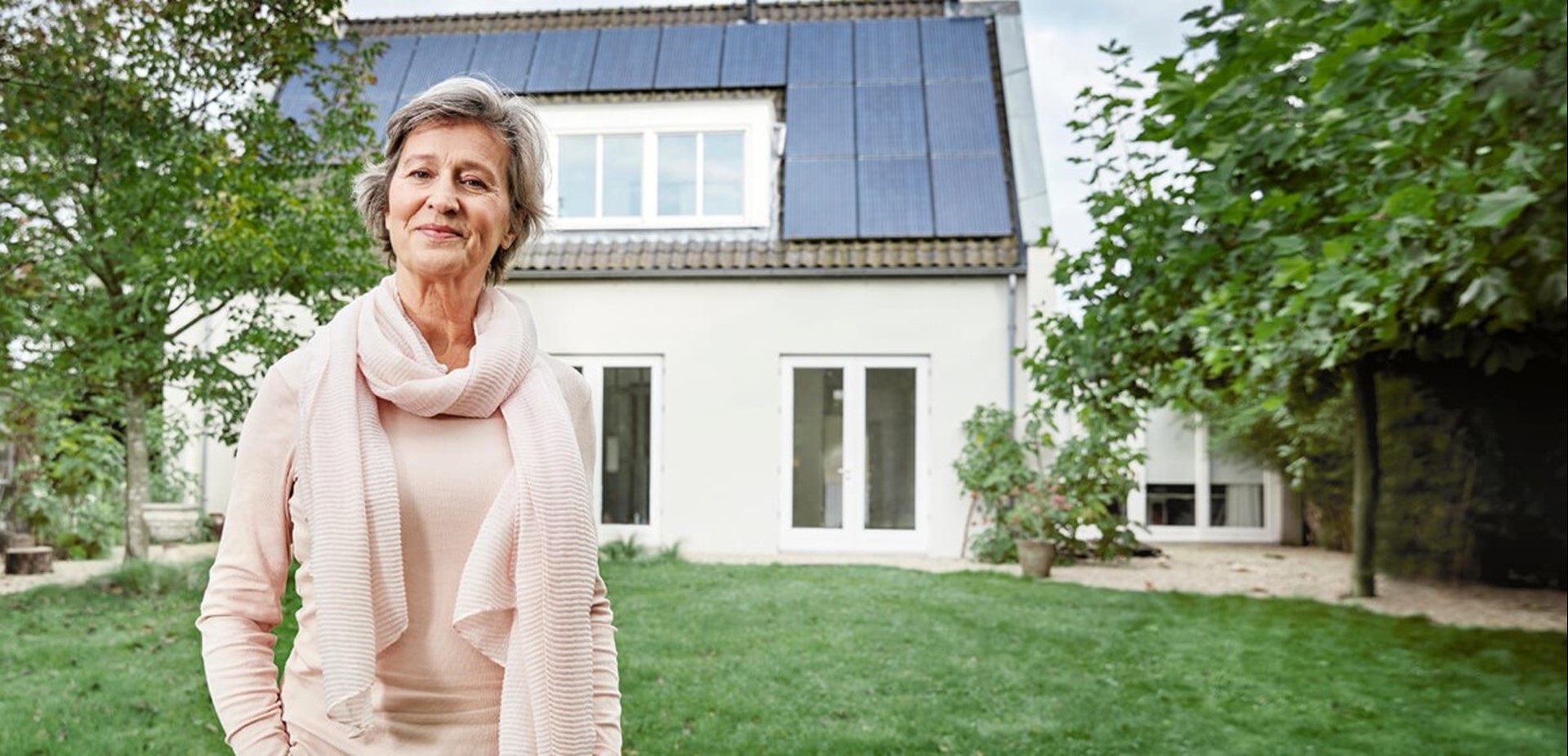 Mevrouw staat in tuin voor een huis met zonnepanelen