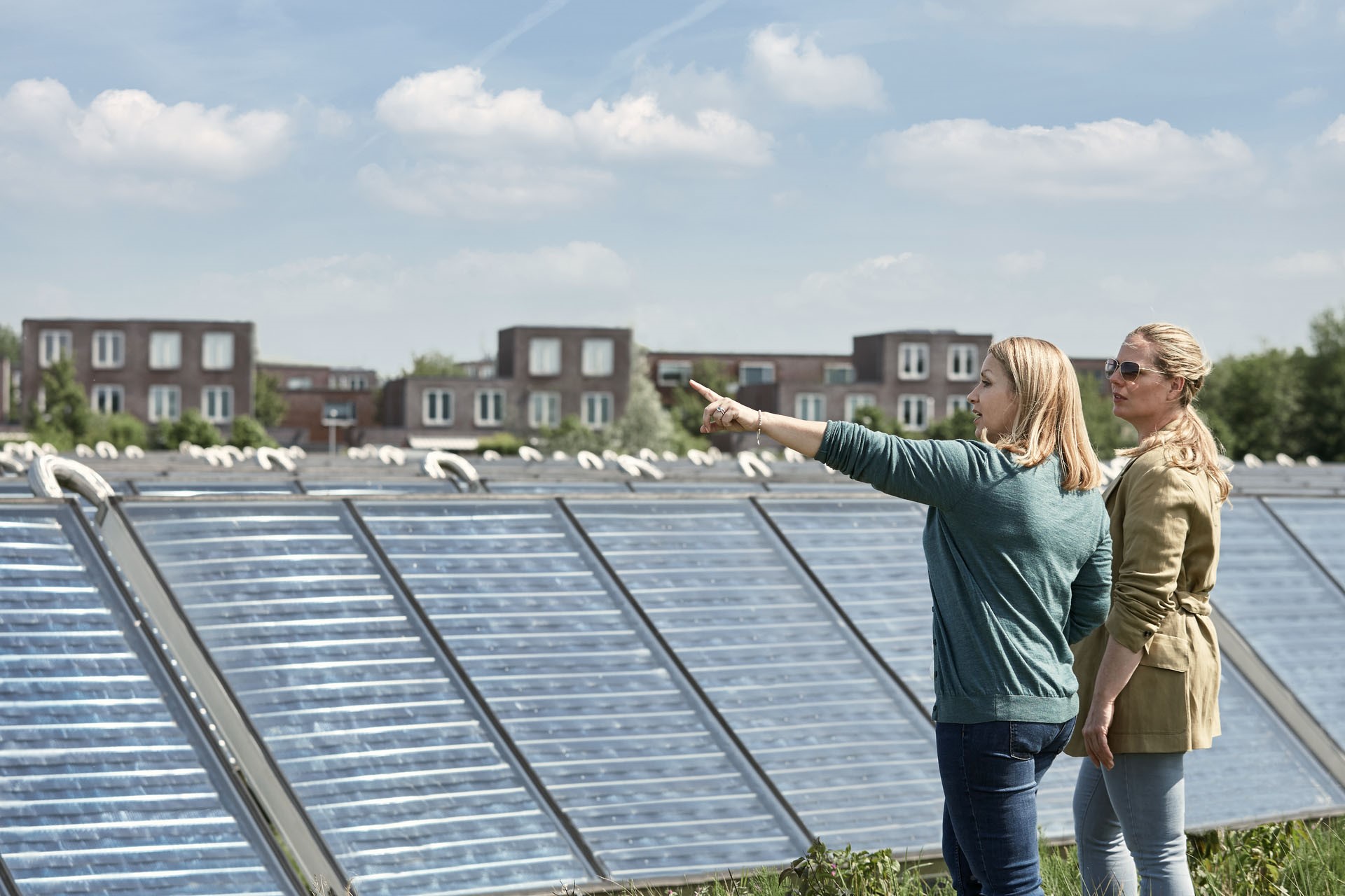 Twee vrouwen op een dak naast zonnepanelen | Postcoderoosregeling