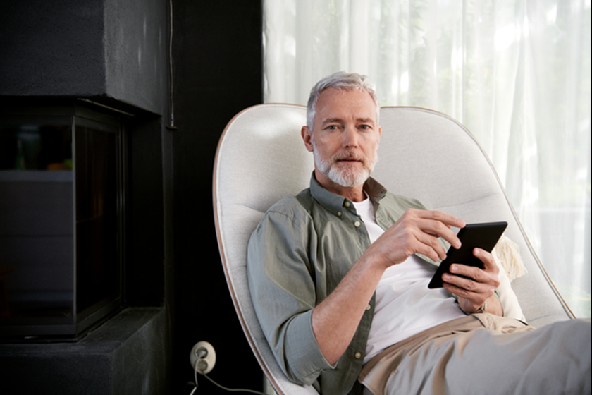 Man met grijs haar zin in een luie stoel met zijn tablet
