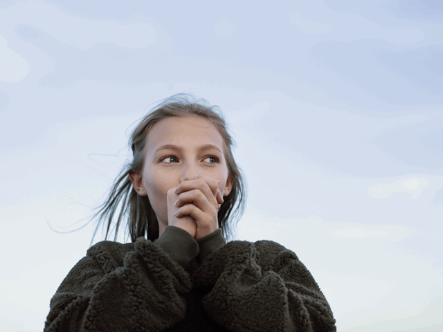 Meisje met bruine trui blaast in haar handen om het warm te krijgen - Meer over stadswarmte