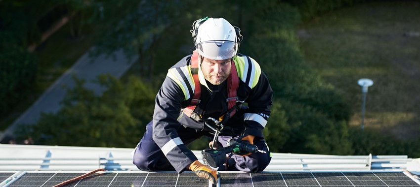 Een van de ervaren installeurs van zonnepanelen aan het werk op dak, met helm en gezekerd