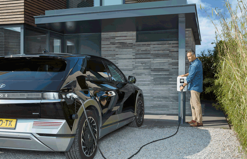 Man met elektrische auto en laadpaal op oprit