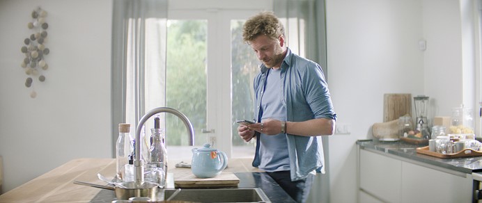 Vlotte man in keuken bekijkt op mobiel energiebesparende klusfilmpjes